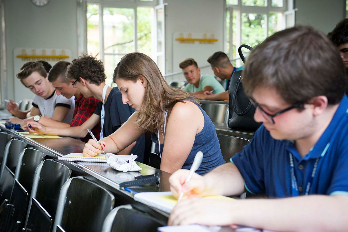 Studierende sitzen in einem Hörsaal und schreiben in ihre Notizbücher.