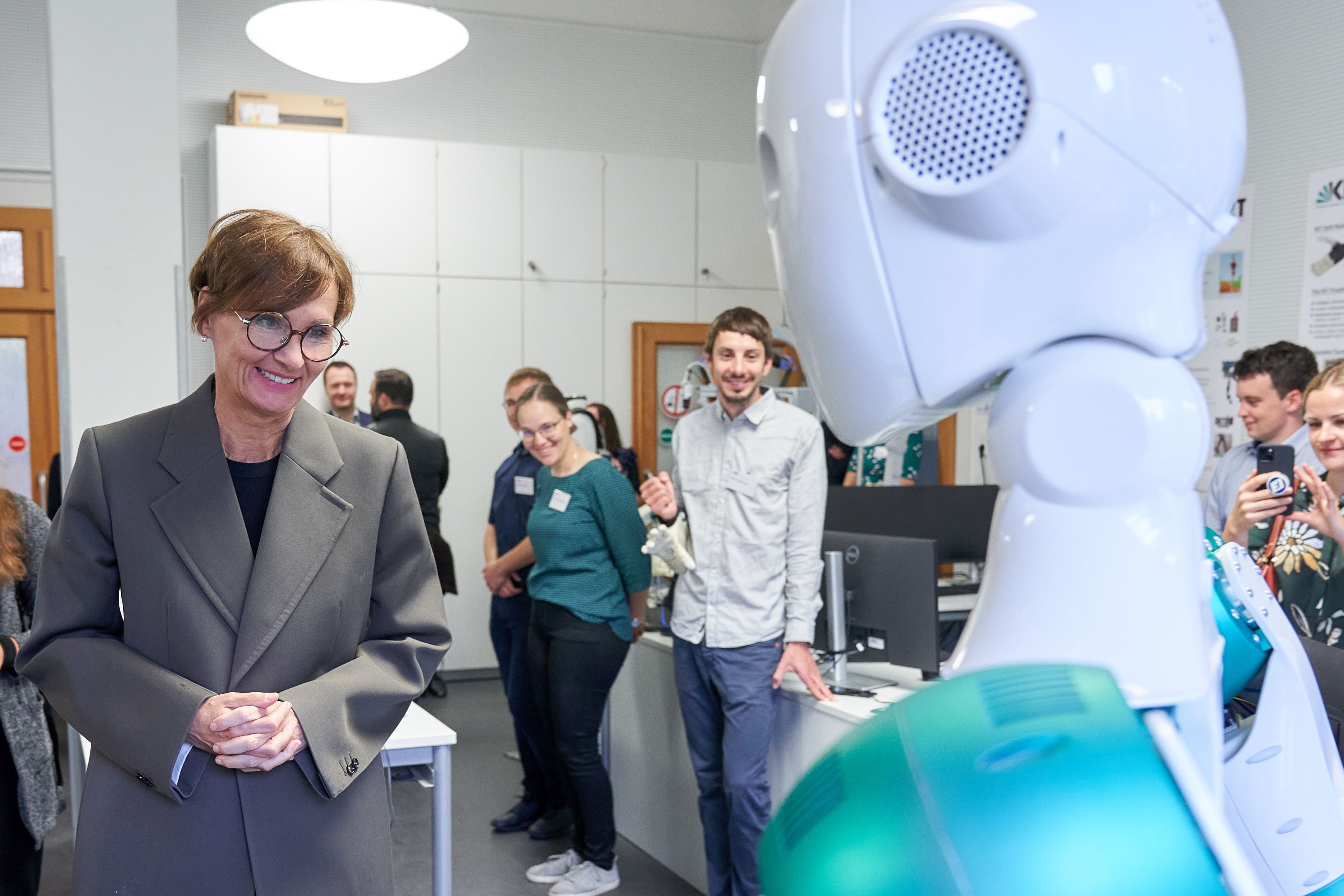 Bild von Bettina Stark-Watzinger, wie sie vom humanoiden Roboter ARMAR-6 begrüßt wird