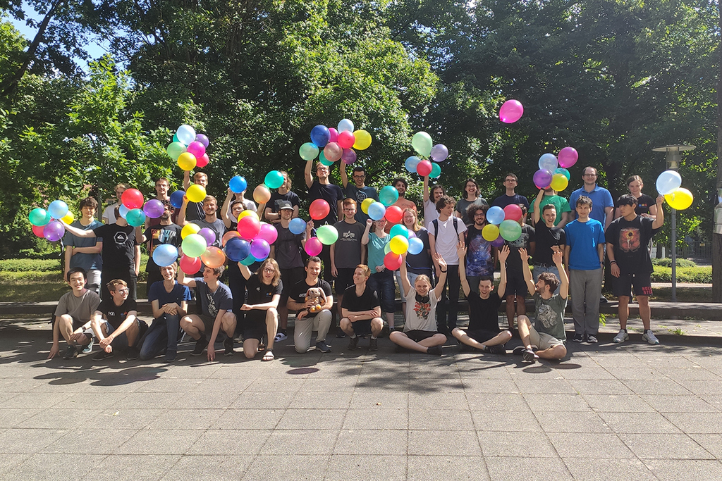 Group photo of people holding colorful balloons outdoors.