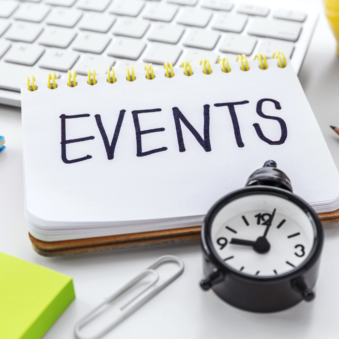 Notizblock mit dem Wort „EVENTS“ neben Stoppuhr und Bürobedarf auf Schreibtisch.